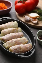 Photo of Uncooked stuffed cabbage rolls and ingredients on grey table