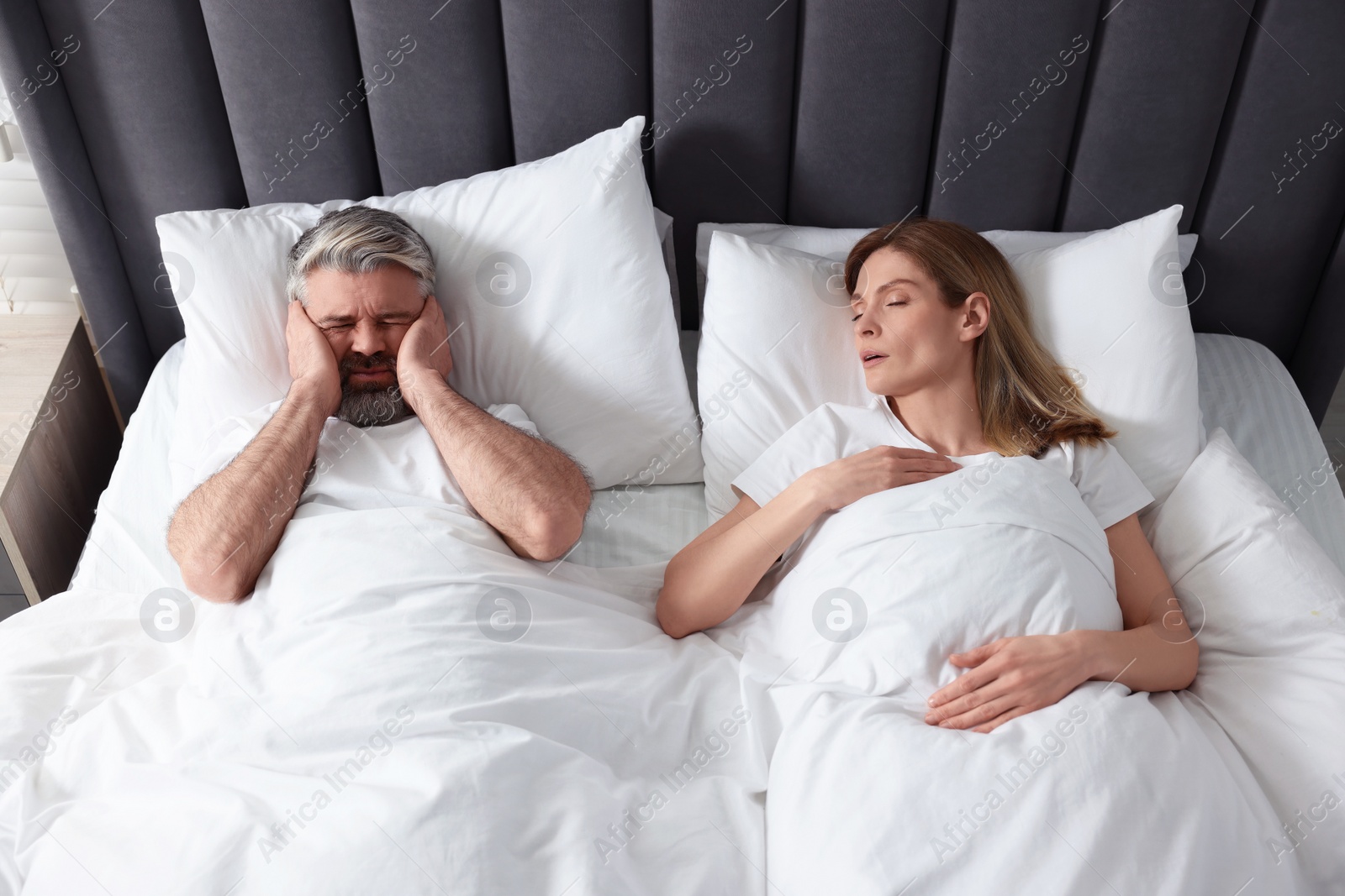 Photo of Irritated man lying near his snoring wife in bed at home