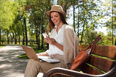 Photo of Woman with smartphone working on laptop in park