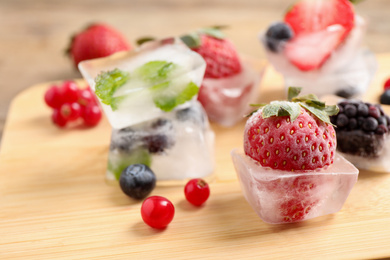 Photo of Ice cubes with different berries and mint on wooden board, closeup