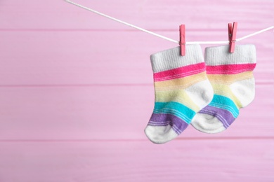 Photo of Pair of socks on laundry line against pink wooden background, space for text. Baby accessories