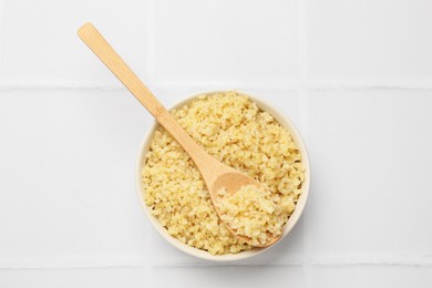 Photo of Delicious bulgur served on white tiled table, top view