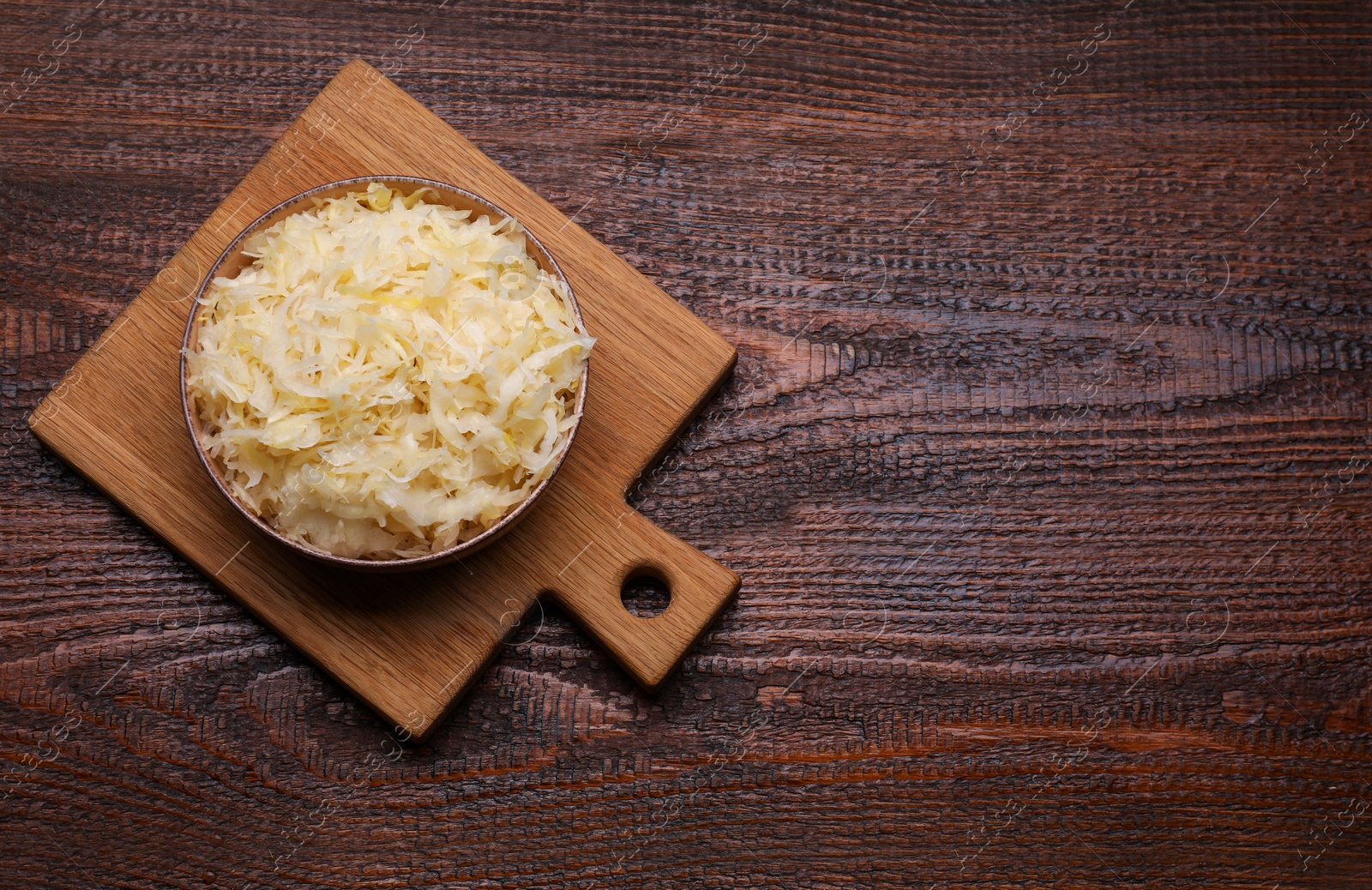 Photo of Bowl of tasty sauerkraut on wooden table, top view. Space for text