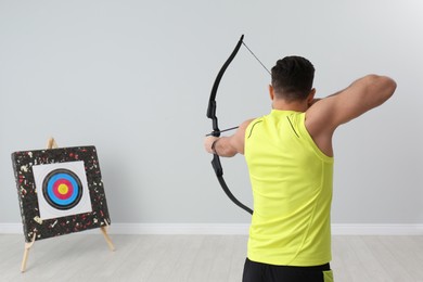 Man with bow and arrow aiming at archery target indoors