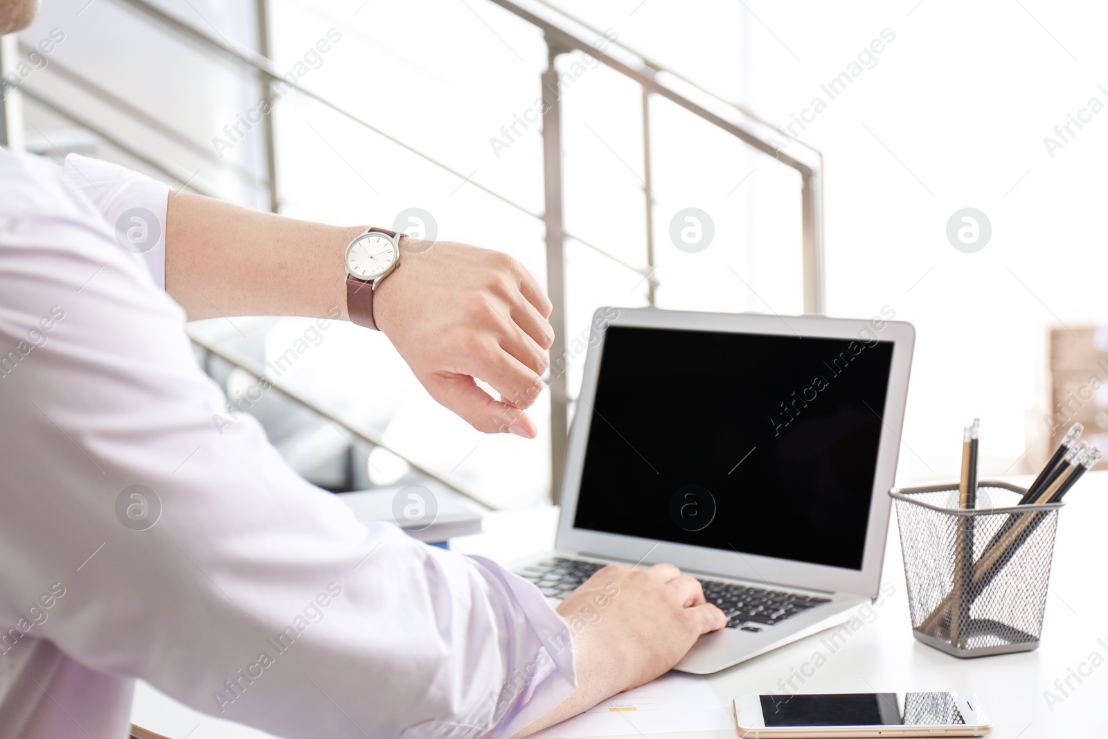 Photo of Young businessman checking time on his wristwatch at workplace. Time management