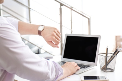 Photo of Young businessman checking time on his wristwatch at workplace. Time management