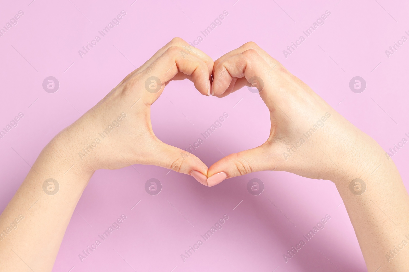 Photo of Woman showing heart gesture with hands on pink background, closeup