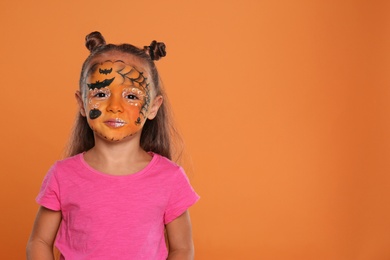 Photo of Cute little girl with face painting on orange background. Space for text