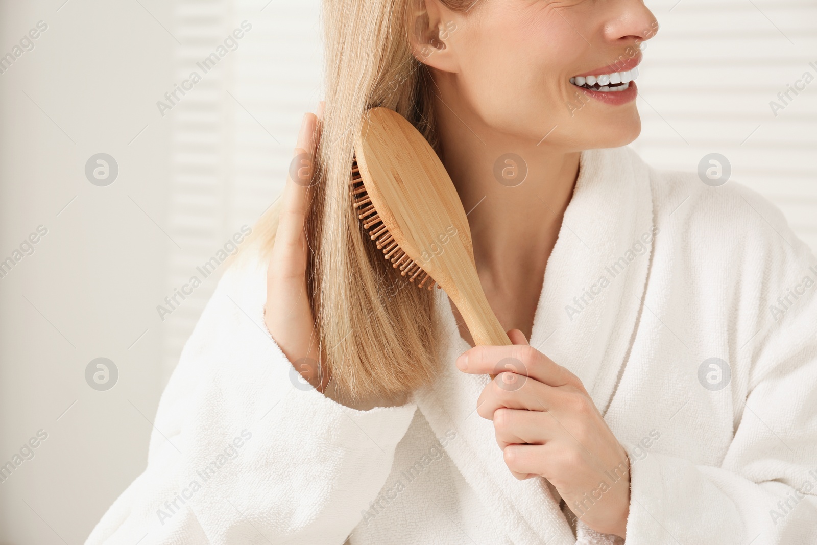 Photo of Woman in white robe brushing her hair indoors, closeup