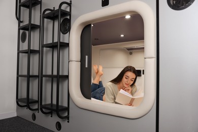 Photo of Young woman reading book in capsule of pod hostel