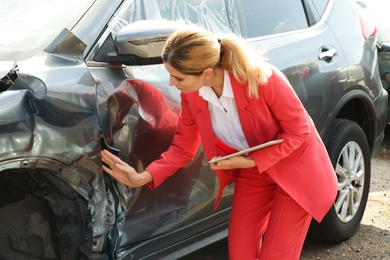 Photo of Insurance agent with tablet inspecting broken car after accident