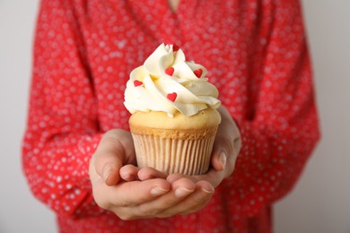 Woman holding tasty cupcake for Valentine's Day on light grey background, closeup