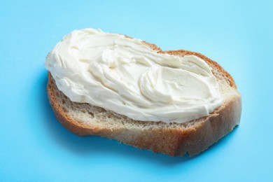 Photo of Slice of bread with tasty cream cheese on light blue background, closeup