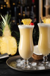 Photo of Tasty Pina Colada cocktails and ingredients on black wooden bar countertop