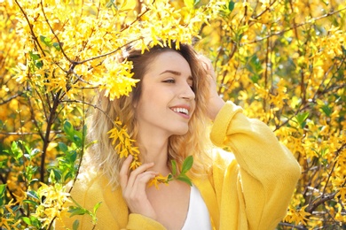 Attractive young woman posing near blossoming bush on sunny spring day