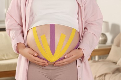 Photo of Pregnant woman with kinesio tapes on her belly at home, closeup