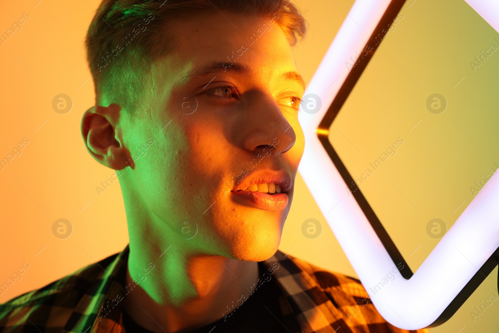 Photo of Young man with square lamp on color background in neon lights