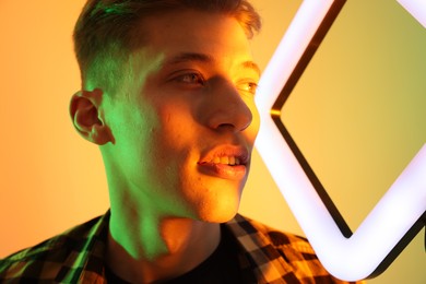 Young man with square lamp on color background in neon lights