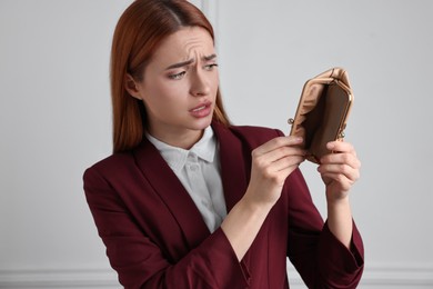 Photo of Upset woman with empty wallet near white wall