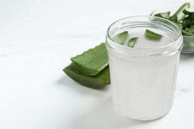 Photo of Fresh aloe juice in jar and leaves on white marble table, closeup. Space for text