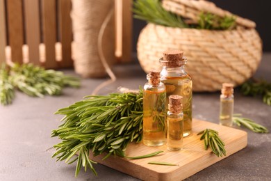 Photo of Essential oil in bottles and rosemary on grey table