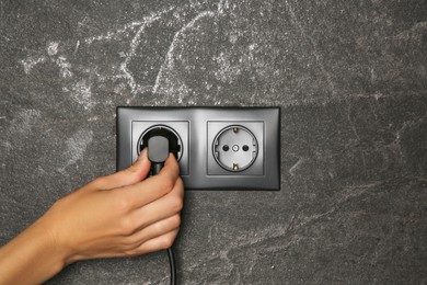 Photo of Woman putting plug into socket indoors, closeup