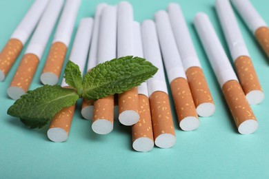 Photo of Menthol cigarettes and mint on turquoise background, closeup