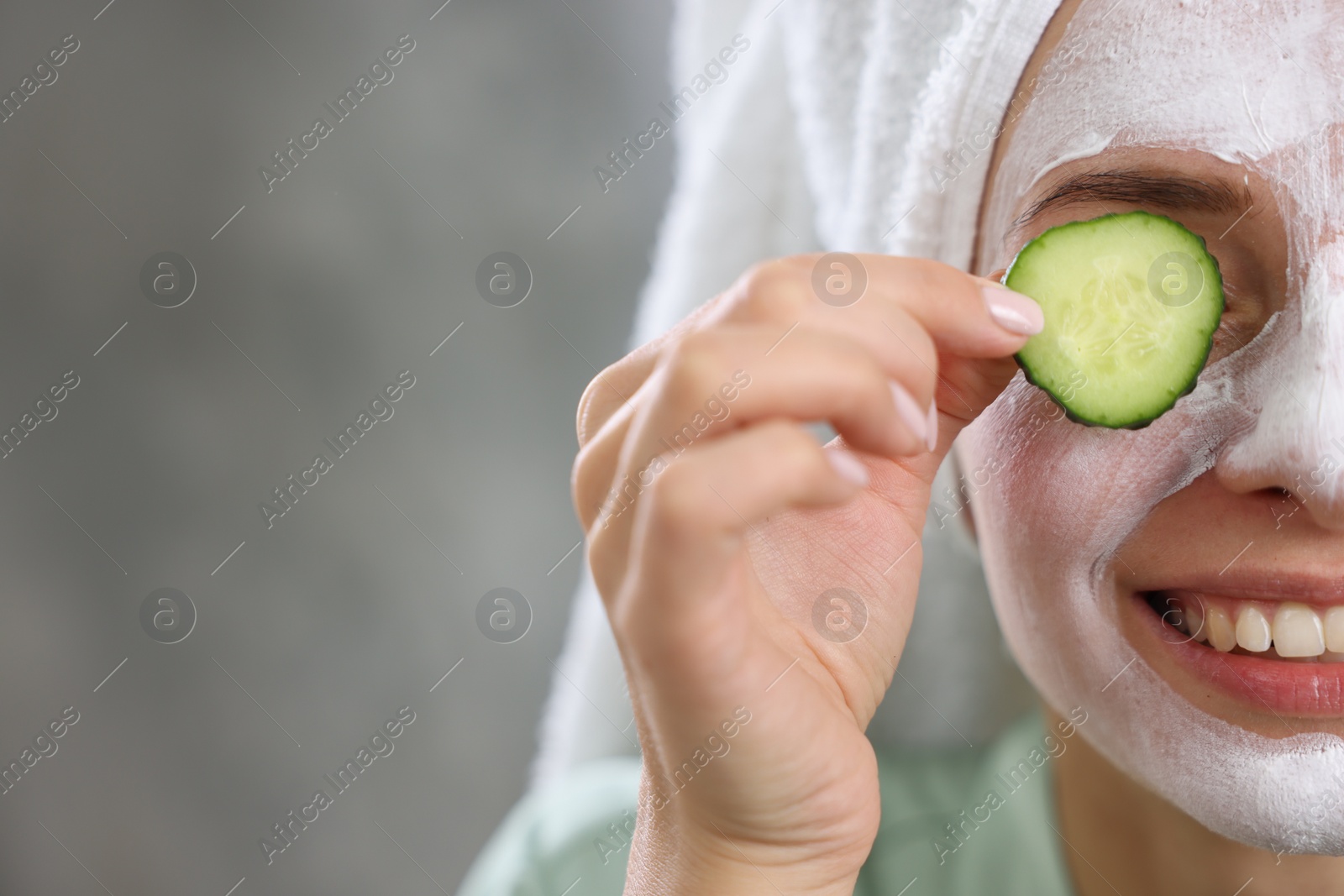 Photo of Woman with face mask and cucumber slice on blurred background, closeup and space for text. Spa treatments