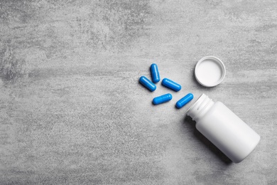 Photo of Container with blue capsules on grey background