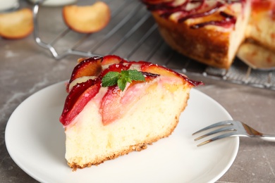 Photo of Slice of delicious cake with plums on grey marble table, closeup