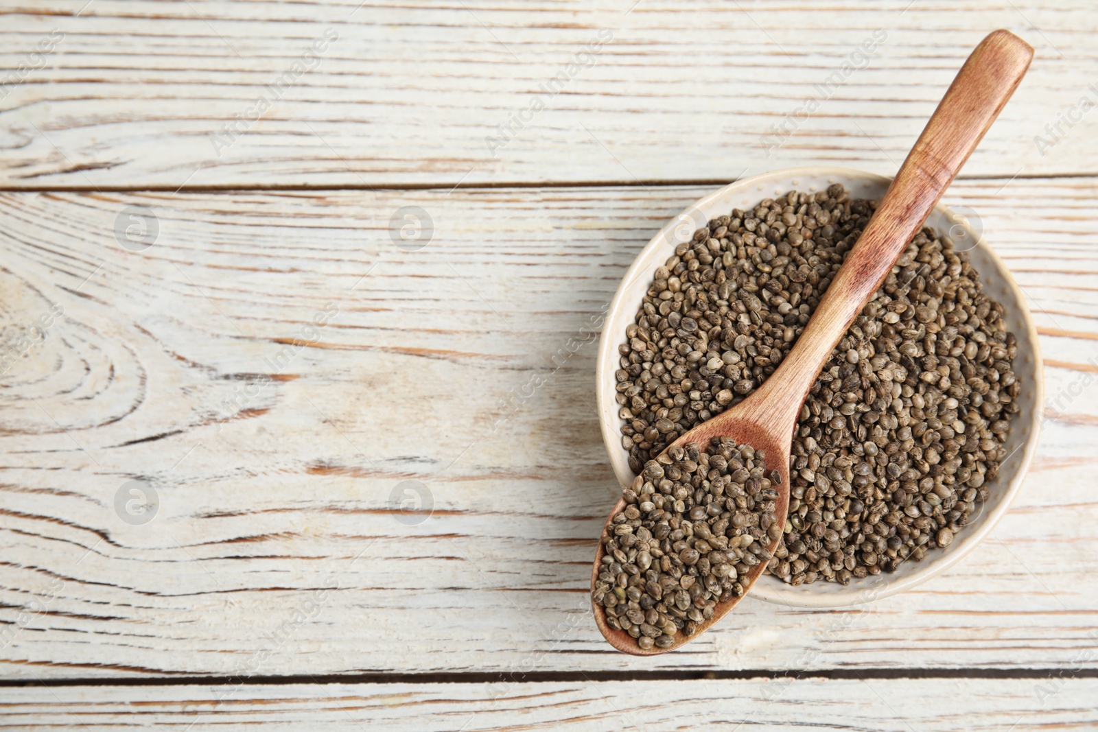 Photo of Bowl and spoon with organic hemp seeds on white wooden table, top view. Space for text