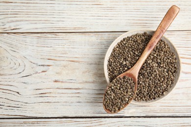 Bowl and spoon with organic hemp seeds on white wooden table, top view. Space for text