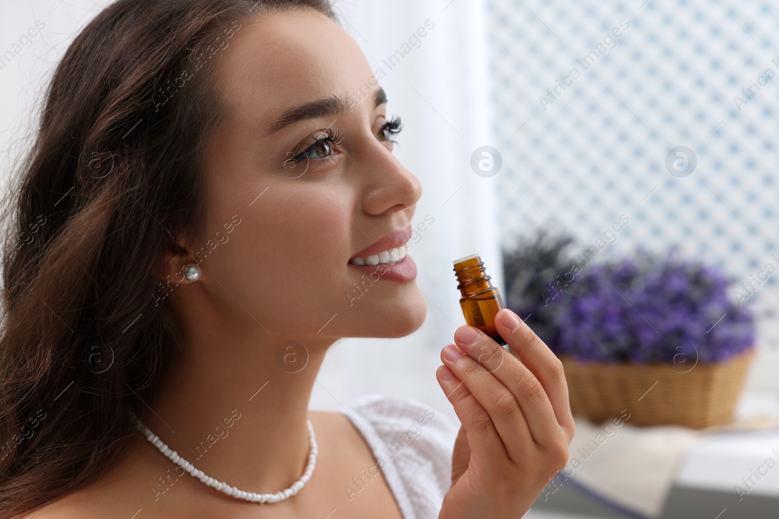 Photo of Beautiful happy woman with bottle of essential oil indoors