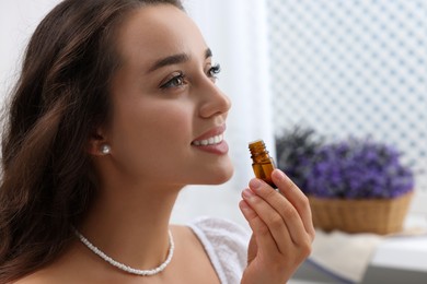 Beautiful happy woman with bottle of essential oil indoors