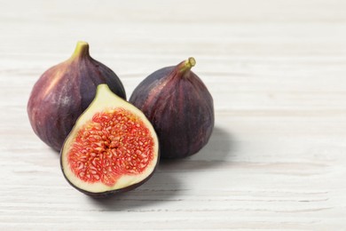 Photo of Whole and cut ripe figs on white wooden table, closeup. Space for text