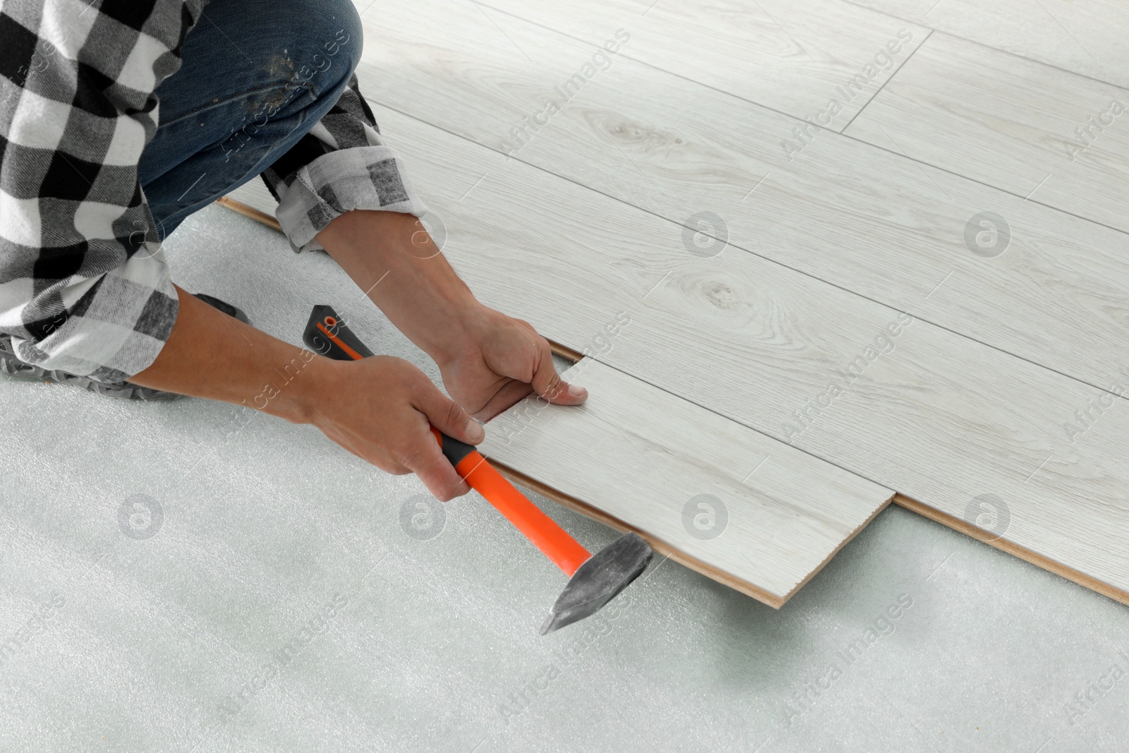 Photo of Professional worker using hammer during installation of new laminate flooring, closeup