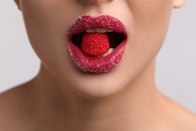 Photo of Young woman with beautiful lips covered in sugar eating candy on light background, closeup