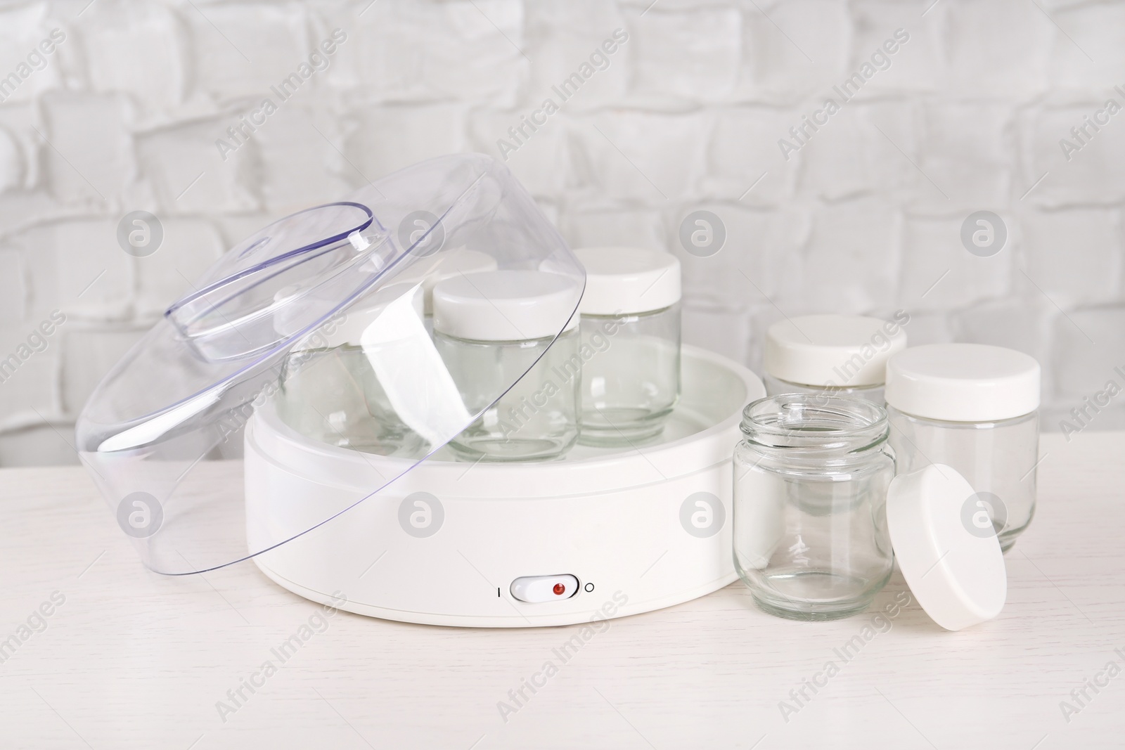 Photo of Modern yogurt maker with empty jars on white wooden table