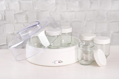 Photo of Modern yogurt maker with empty jars on white wooden table