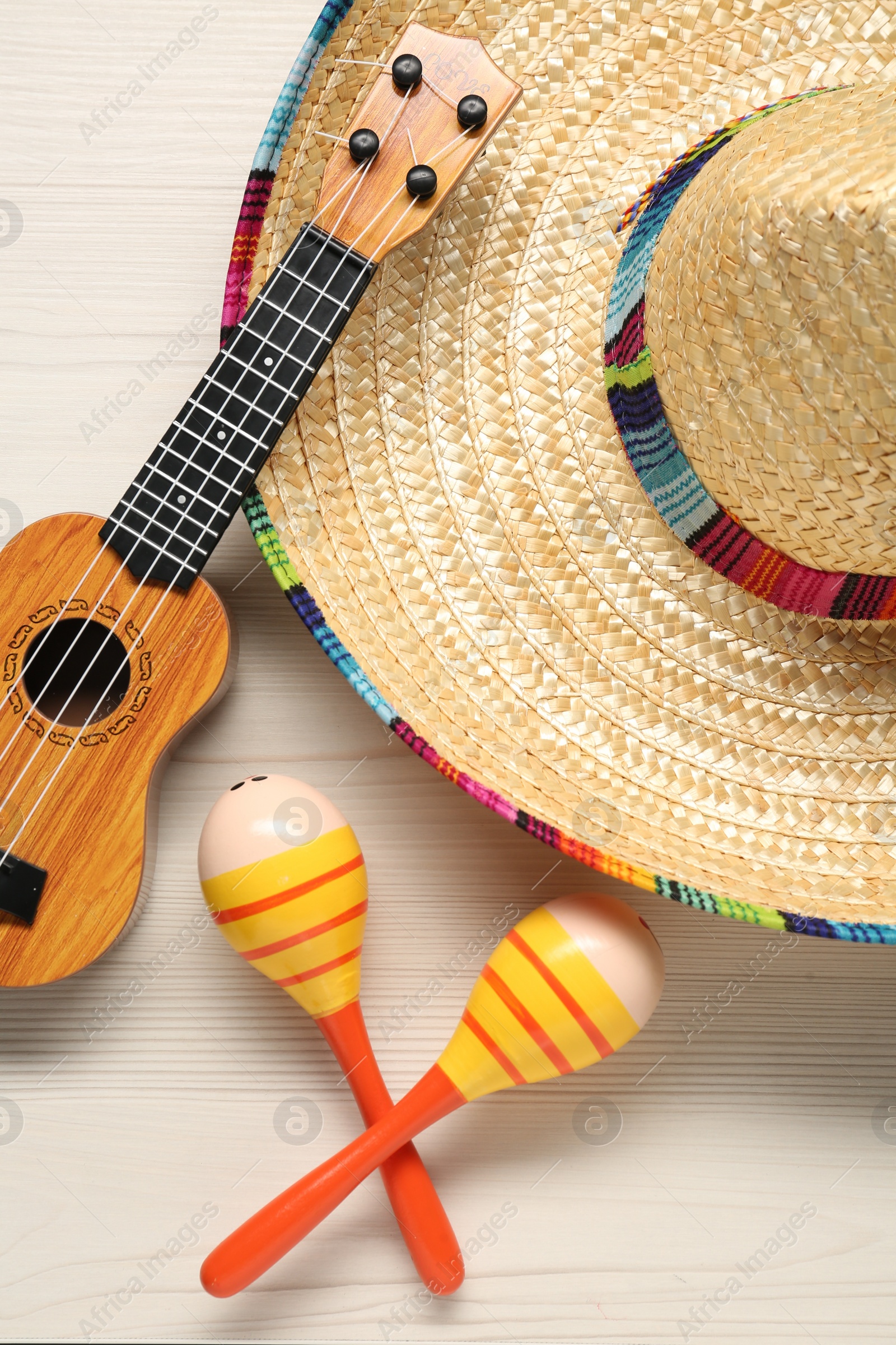 Photo of Mexican sombrero hat, maracas and guitar on white wooden background, flat lay