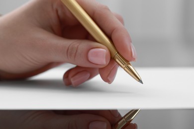 Photo of Woman writing on sheet of paper at glass table, closeup