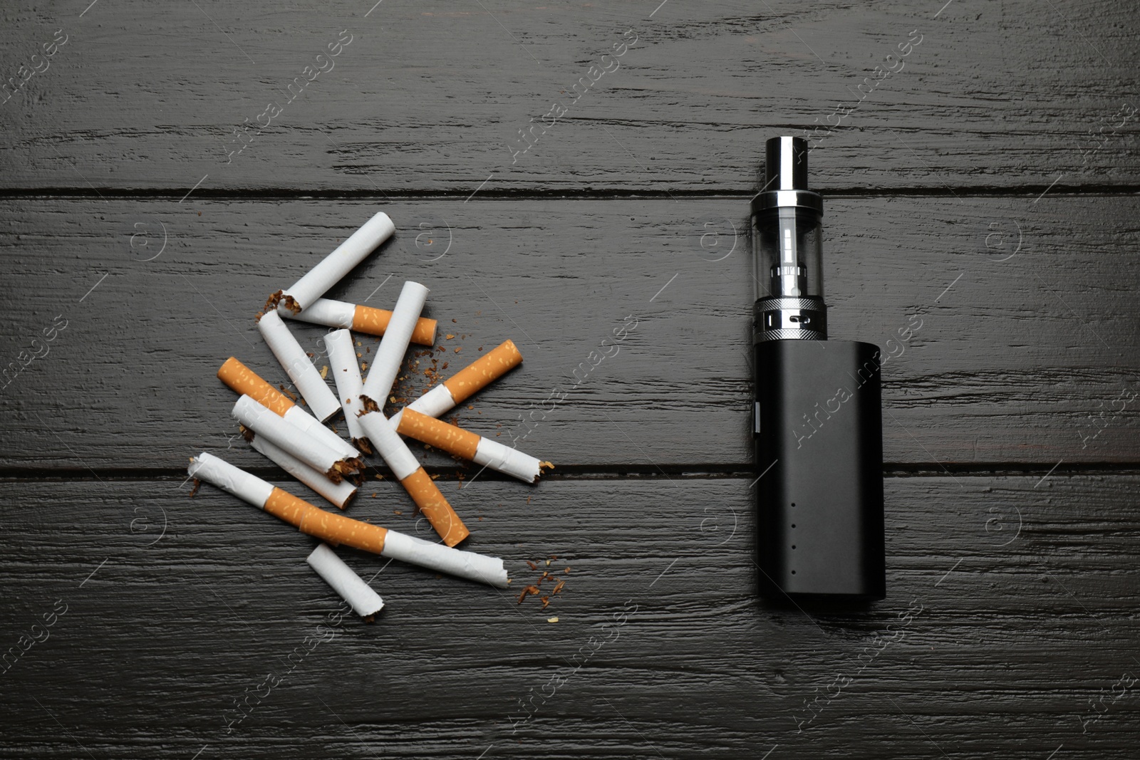 Photo of Broken cigarettes and vaping device on black wooden background, flat lay. Smoking alternative