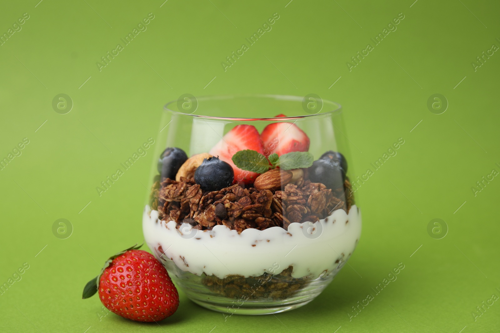 Photo of Tasty granola with berries, nuts and yogurt in glass on green background