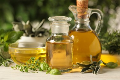 Different fresh herbs with oils on white wooden table, closeup