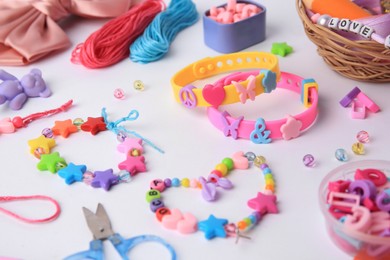 Photo of Kid's handmade beaded jewelry and different supplies on white background, closeup