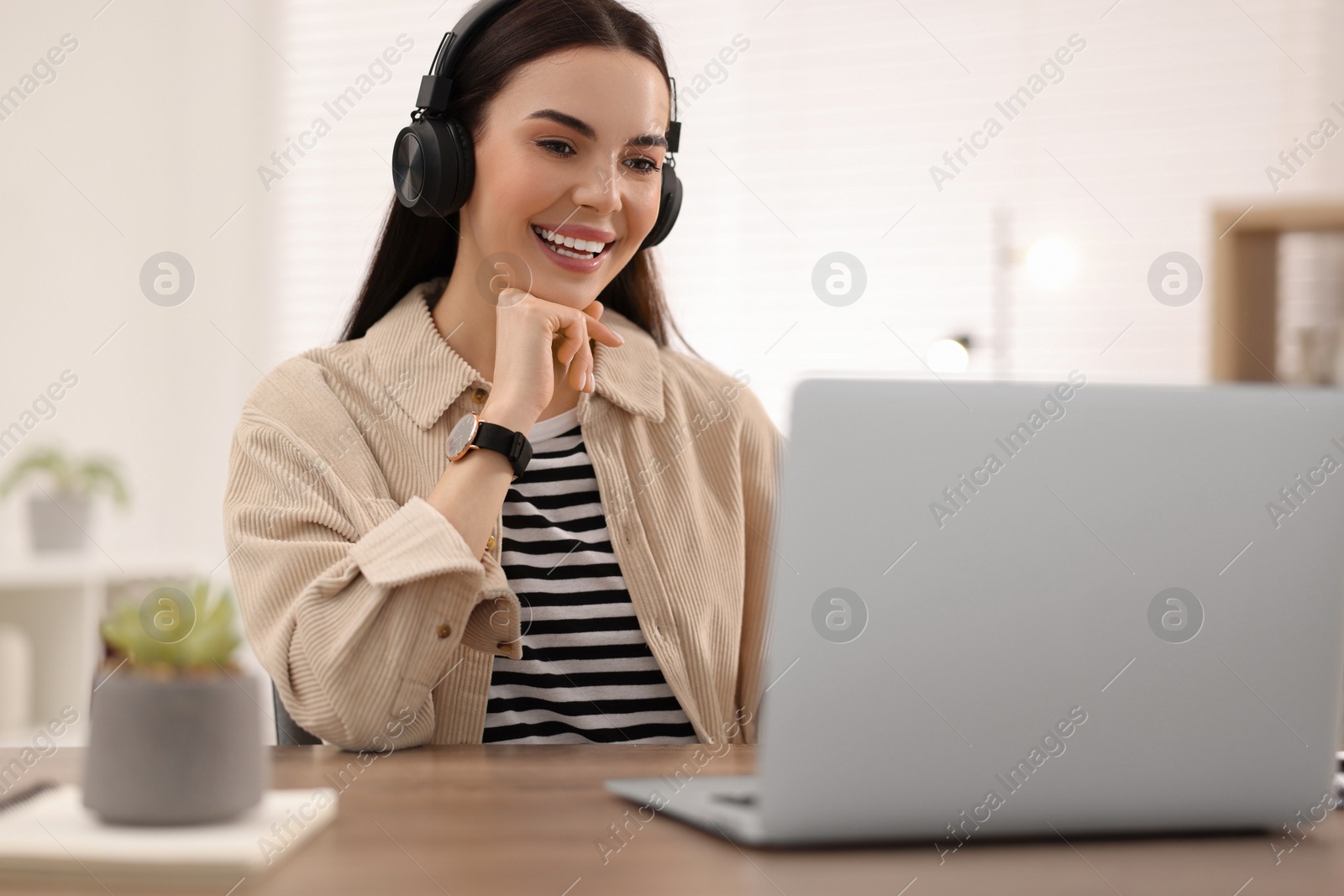 Photo of Young woman in headphones watching webinar at table in room