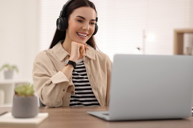 Young woman in headphones watching webinar at table in room