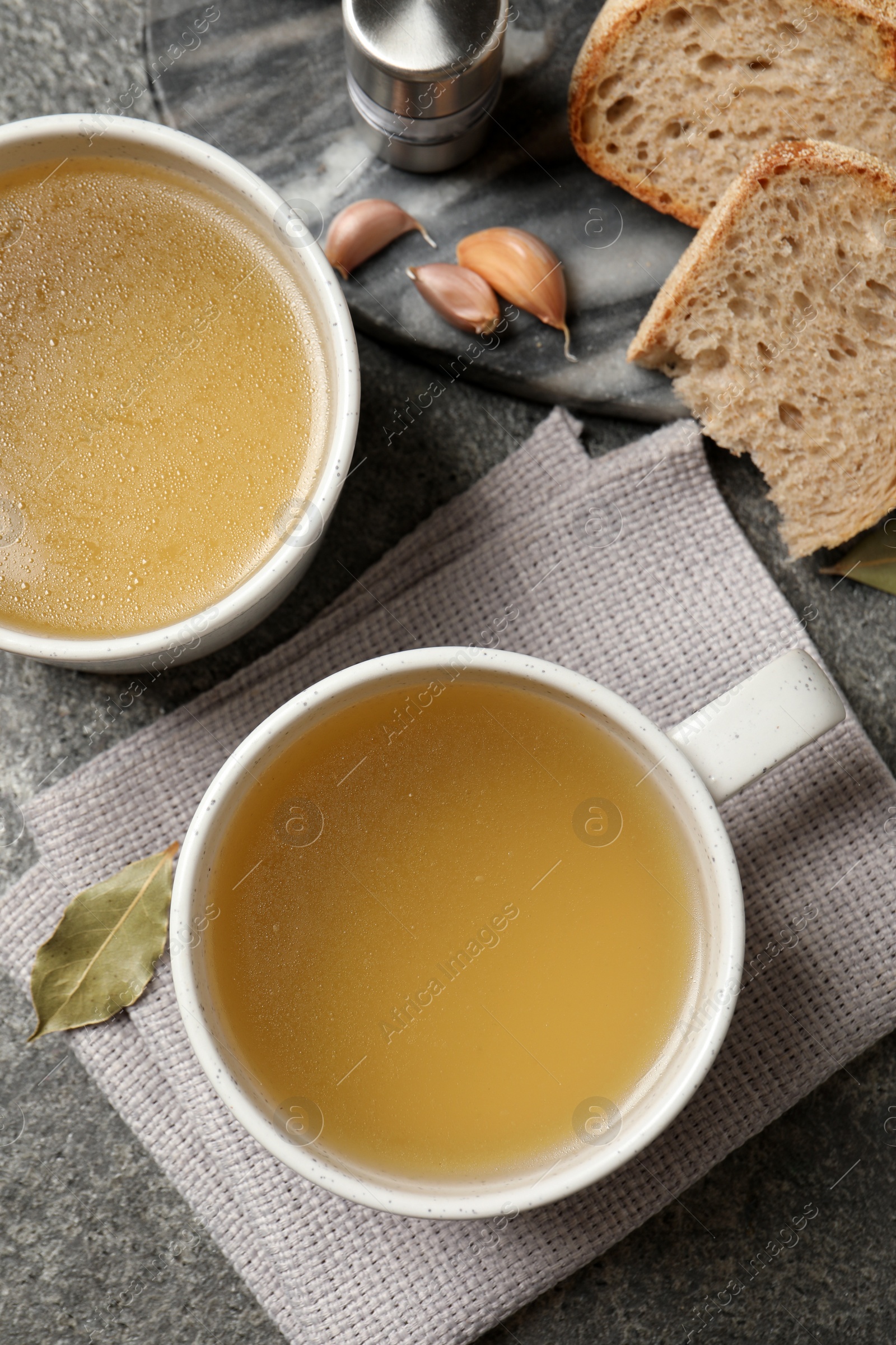 Photo of Hot delicious bouillon in cups on grey table, flat lay