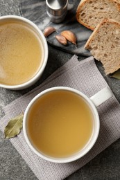 Photo of Hot delicious bouillon in cups on grey table, flat lay