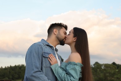 Photo of Romantic date. Beautiful couple kissing against blue sky with clouds